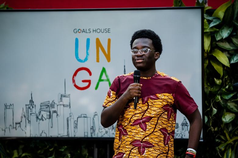 A young Black man speaks into a microphone in front of a backdrop that says UNGA