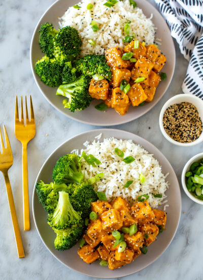 Two plates of air fryer tofu served alongside rice and broccoli.