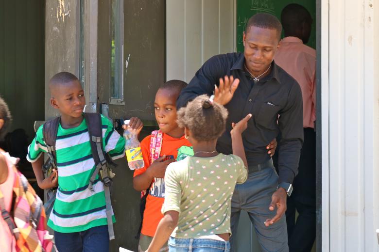 A young Black man in a black shirt high-fives a girl as two other children watch