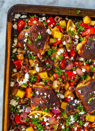 A close-up of baked chicken thighs on a sheet pan with vegetables.