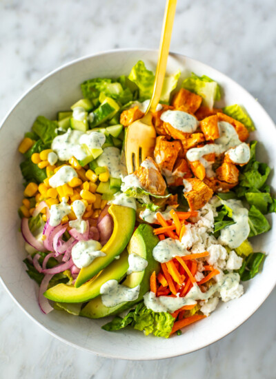 A close-up of a bowl of buffalo chicken salad with ranch dressing drizzled over top.