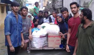 A group of Indian men and women stand with a palate of flood relief supplies