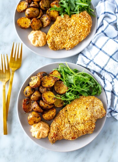 Two plates, each with a chicken cutlet, lemon dill potatoes and a side of arugula.