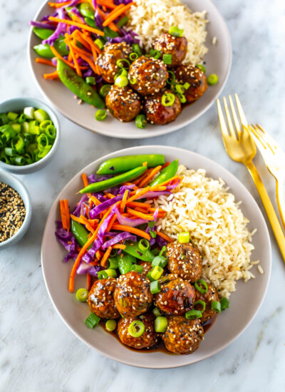 Two bowls with a bed of rice, side of stir fried veggies and sticky teriyaki chicken meatballs.