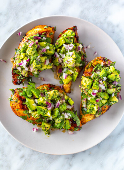 Four cilantro lime chicken cutlets on a plate, each topped with avocado salsa.