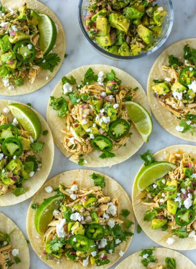 Multiple cilantro lime chicken tacos topped with avocado salsa and feta cheese.