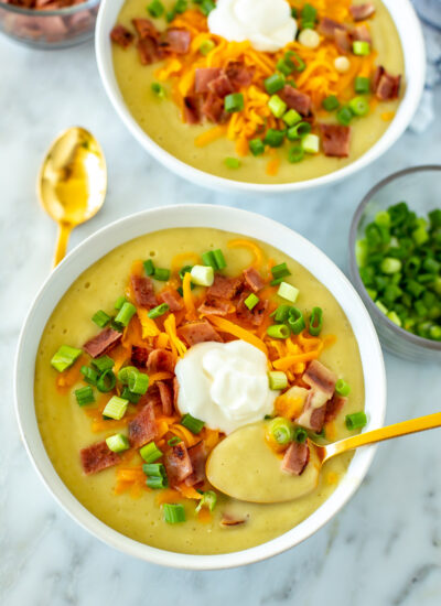 Two bowls of crockpot potato soup with a spoon in the bowl placed in the foregound.