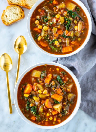 Two bowls of crockpot vegetable soup with spoons on the side.