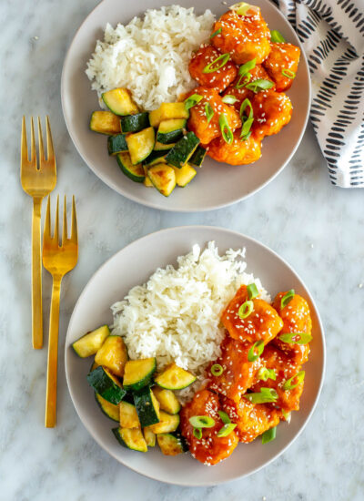 Two plates of firecracker chicken with rice and zucchini.