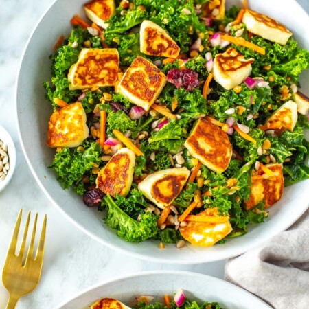 A close-up of a bowl of kale salad topped with halloumi cheese.