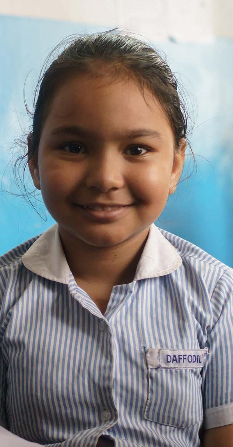 Close up of a young South Asian girl smiling with a painted blue wall in the background