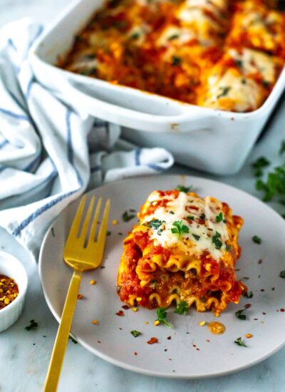 A plate of cheesy spinach lasagna roll-ups topped with melted mozzarella cheese and garnished with fresh basil.