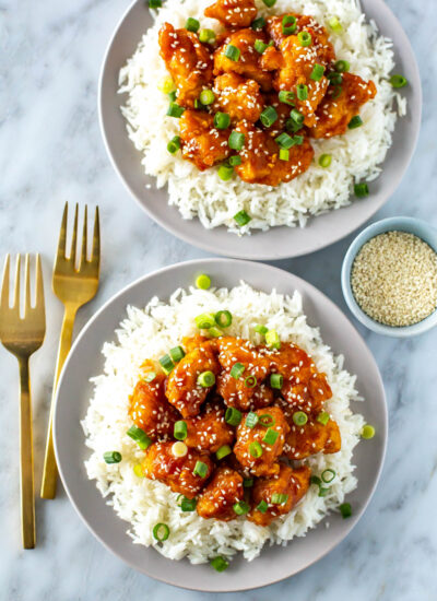 Two plates, each with a bed of rice, topped with crispy mandarin chicken.