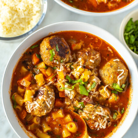 A close-up of Italian turkey meatball soup garnished with parmesan and parsley wth a spoon in it.