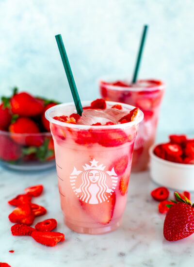 Two cups of homemade Starbucks pink drink with freeze-dried strawberries placed around them.