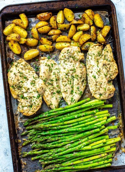 A sheet pan with roasted potatoes, seasoned chicken breasts, and asparagus on top.