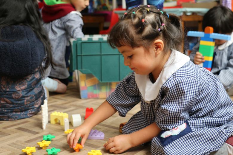 A preschool aged girl in a blue checked dress plays with colorful puzzle pieces on the floor