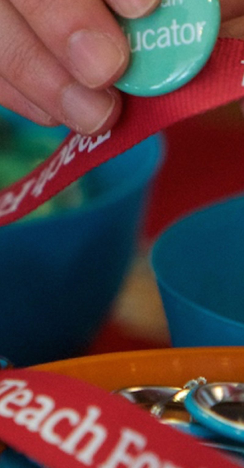 Close-up of a hand pinning a green button to a red Teach For All lanyard